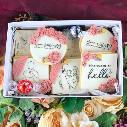 Decorative cookies with floral designs and text in a box, surrounded by flowers.