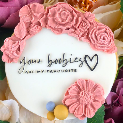 Decorative cake with pink floral decorations and text 'your boobies are my favourite' surrounded by flowers.