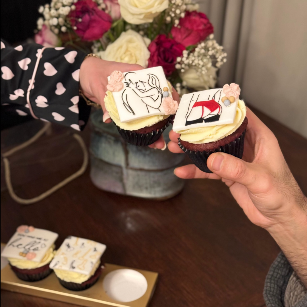 Two people holding cupcakes with artistic designs on a wooden table.