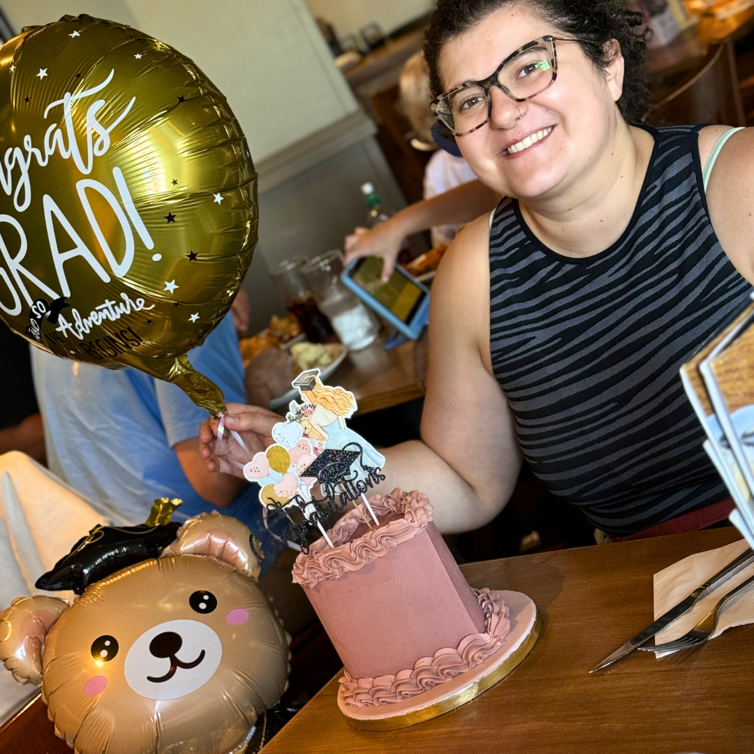 Person holding a 'grats RADI' balloon with a cake and another balloon at a celebration.