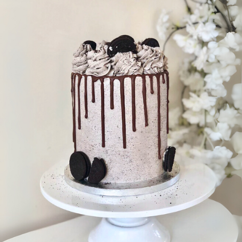 Chocolate cake with chocolate drizzle and cookies on a white stand.