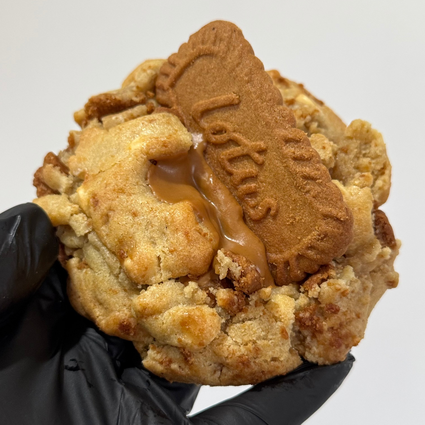 A close-up of a hand wearing a black glove holding a large, crumbly biscuit cookie topped with a piece of caramel and a branded biscuit piece that reads 'Laffy Tiffy'.