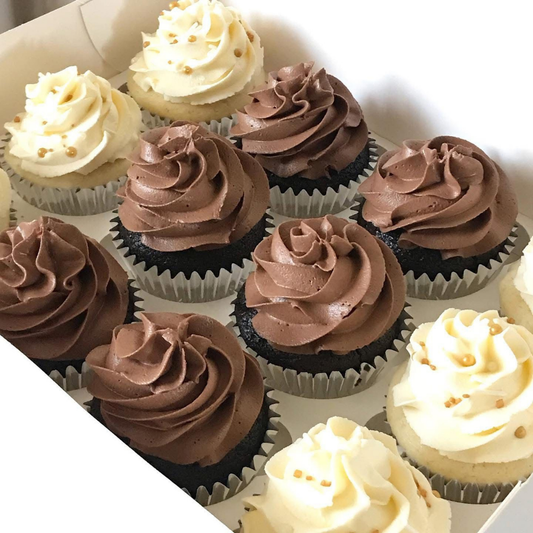An assortment of frosted cupcakes in a white bakery box, featuring swirls of chocolate brown and creamy beige frosting with small sprinkle details.